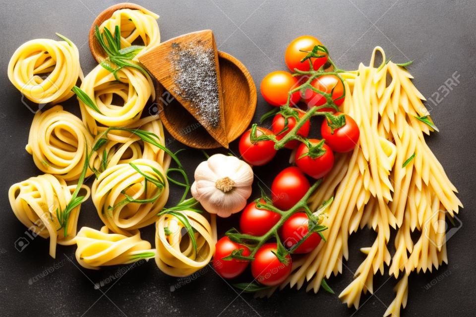 Pasta italiana. Ingredientes para cozinhar massas em fundo escuro, vista superior. Pasta, tomate, alho, pimentão de alecrim