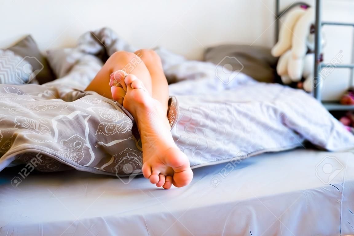 legs of young woman peek out from under covers. lying in bed under warm blanket in hot weather, sound sleep, children's healthy sleep, circadian rhythms concept.