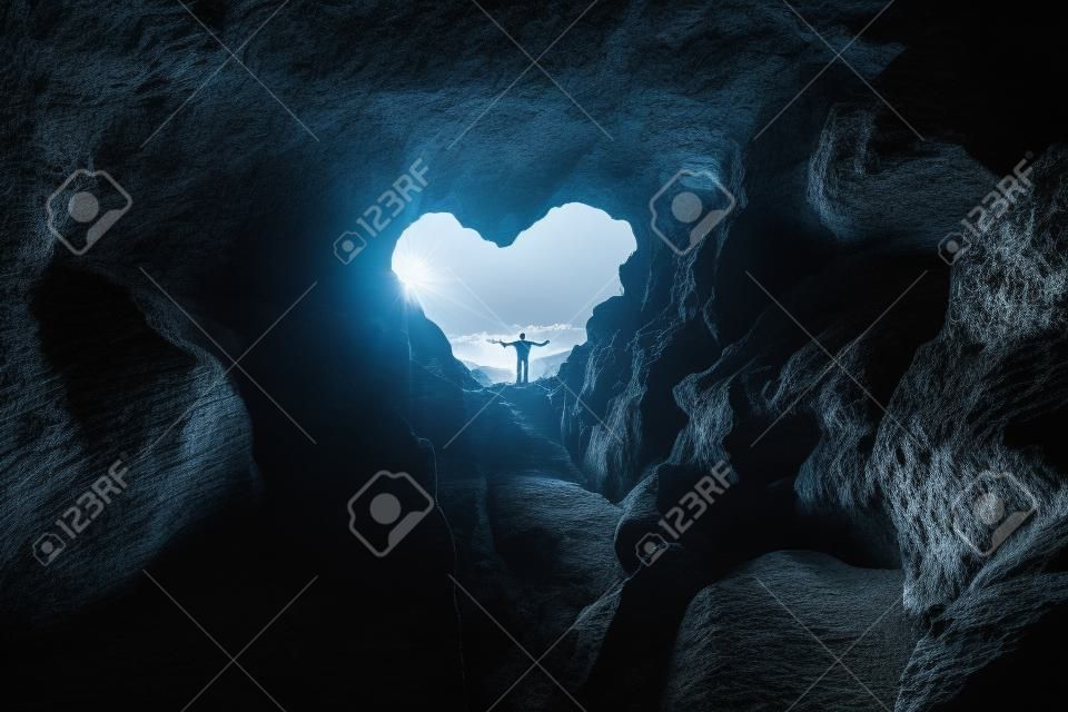 Man stands at heart-shaped opening of a cave and spreads arms
