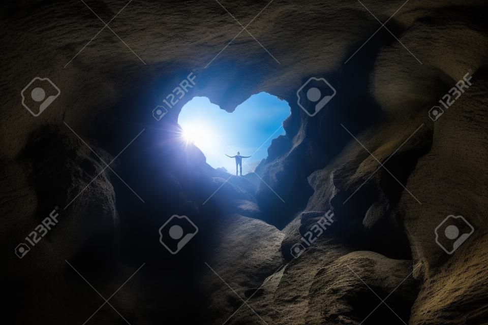 L'homme se tient à l'ouverture en forme de coeur d'une grotte et écarte les bras