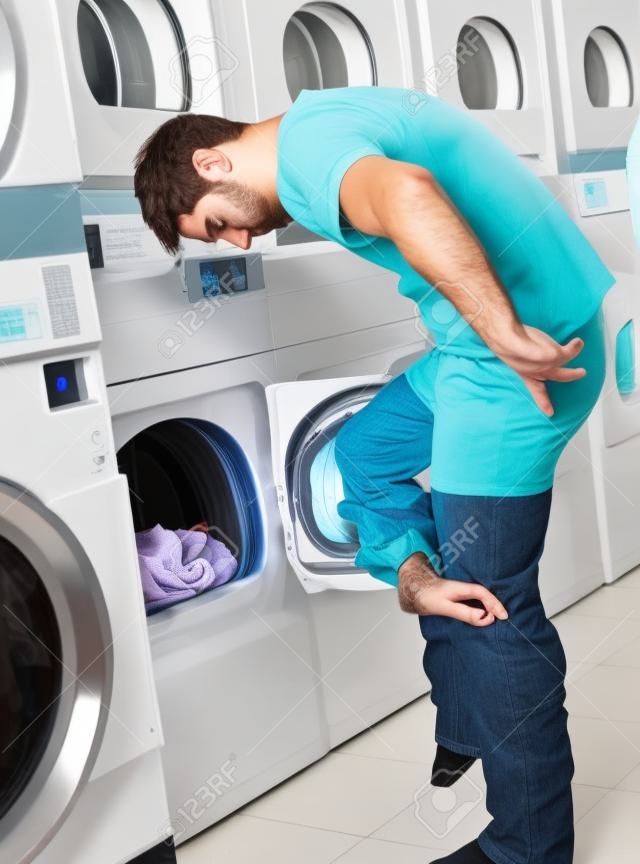Young man undressing his clothes in front of washing machine at laundry