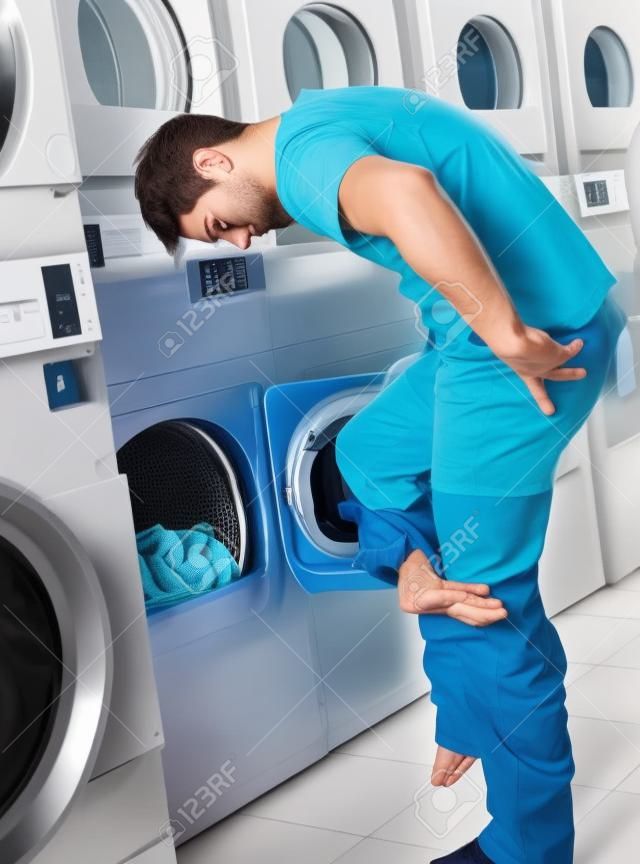 Young man undressing his clothes in front of washing machine at laundry
