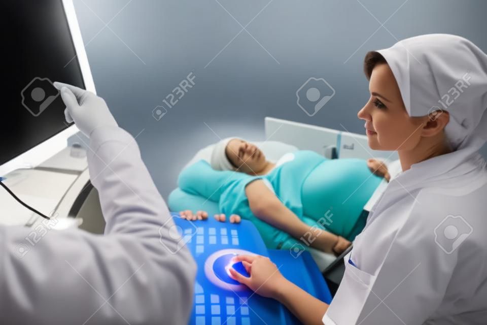 Obstetricians looking at ultrasound monitor while examining pregnant woman in clinic