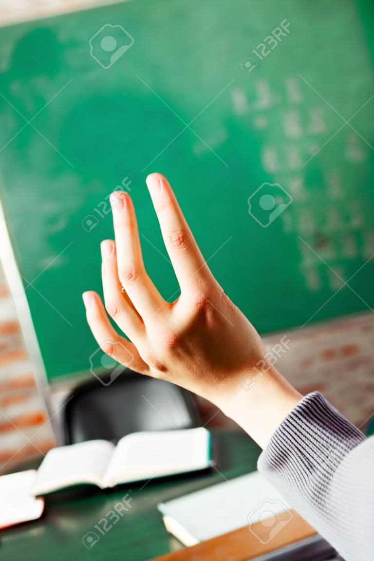 Recorta la imagen de la mano de los estudiantes contra la pizarra verde en el aula