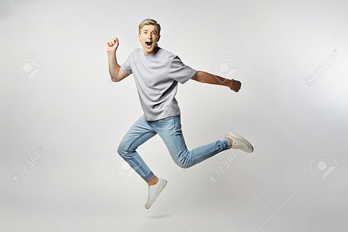 Joyful blond guy dressed in a white t-shirt and jeans happily jumping on the white background in the studio