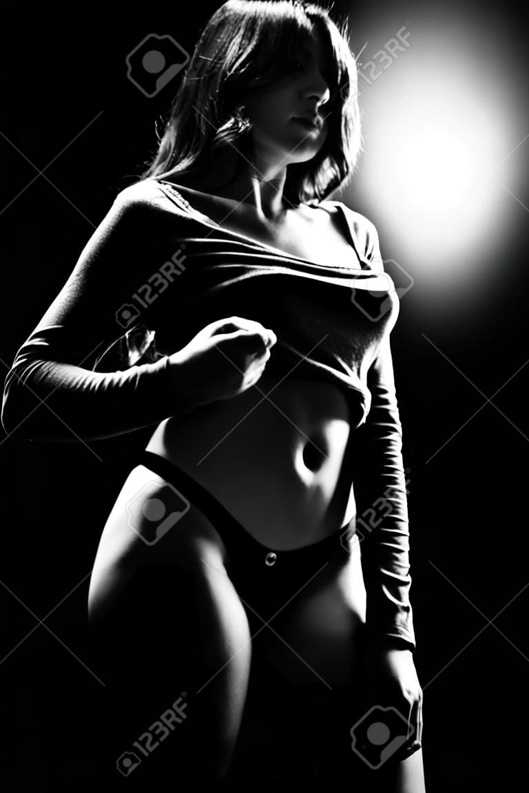 beautiful girl undressing on black background, monochrome