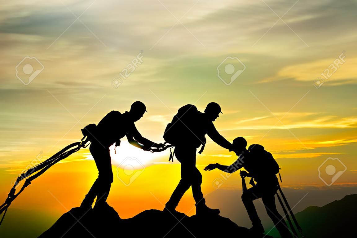 山登りのピーク時のグループは、チームが日没の背景で作業を支援し、旅行トレッキング成功ビジネスコンセプト