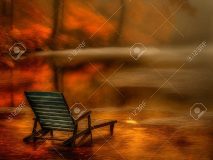 old wooden deck chair on a pond shore in a moody autumn rainy day