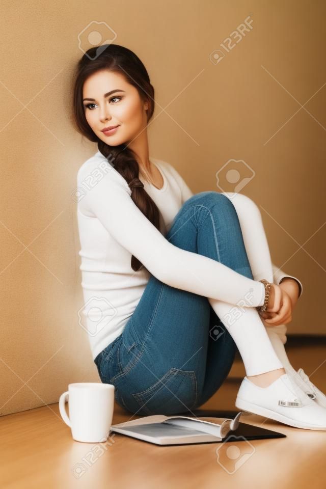 Bella donna seduta sul pavimento e tenendo una tazza. Bella donna