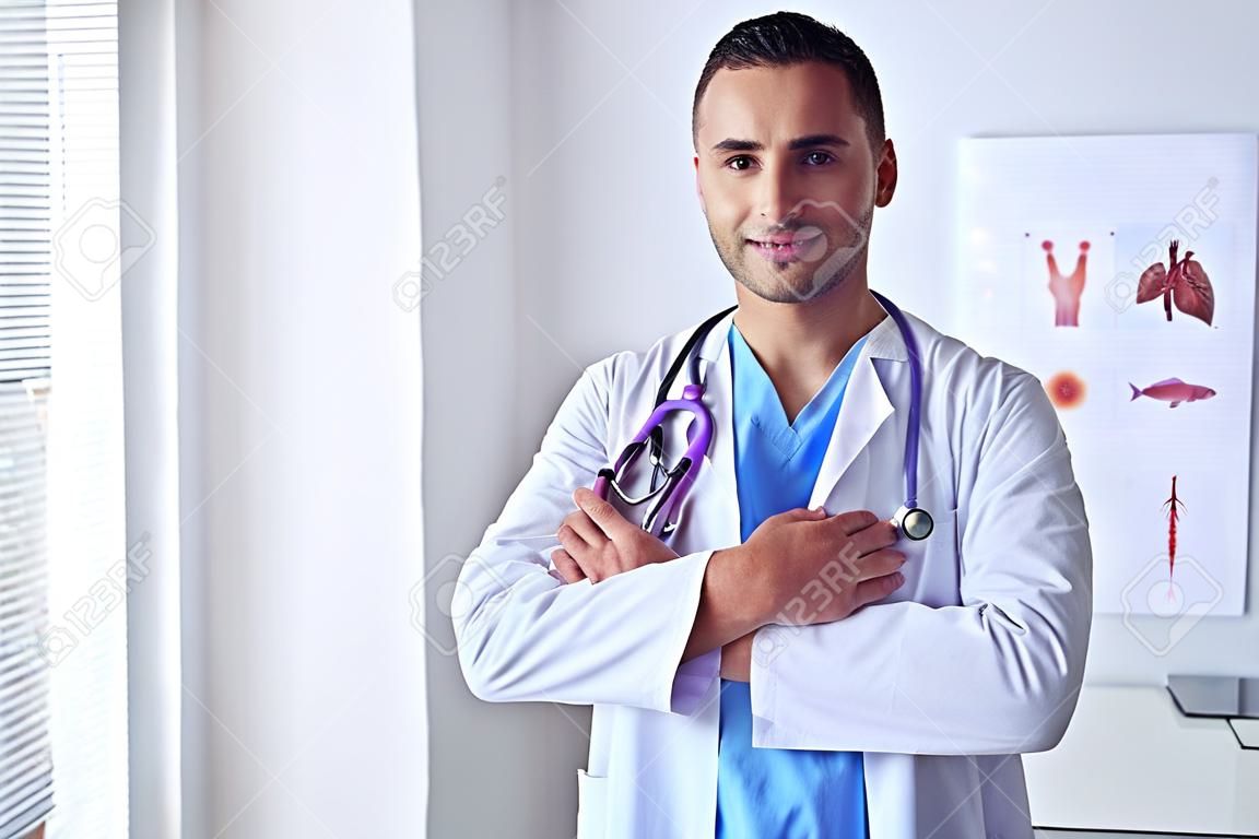 Jonge en zelfverzekerde mannelijke arts portret staande in medisch kantoor.