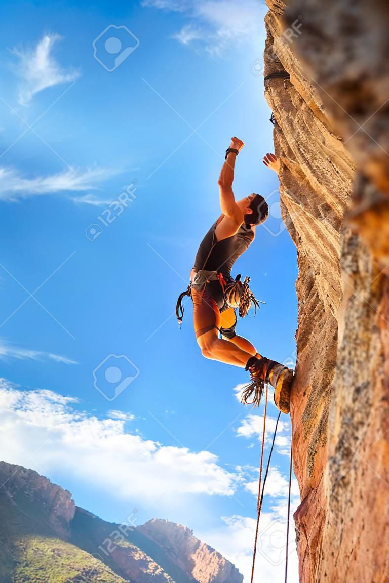Mannelijke rotsklimmer aan de muur tegen de blauwe lucht en bergen. Actief leven, levensstijl en sport concept - stock foto.