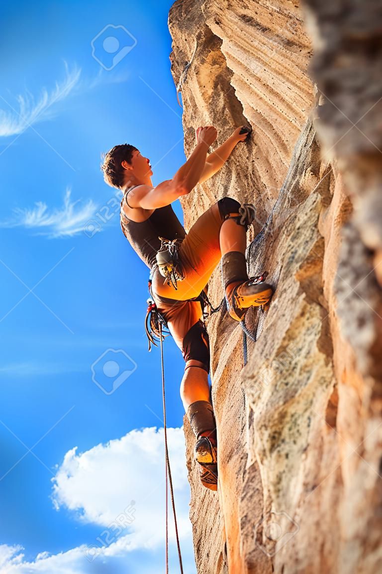 Mannelijke rotsklimmer aan de muur tegen de blauwe lucht en bergen. Actief leven, levensstijl en sport concept - stock foto.