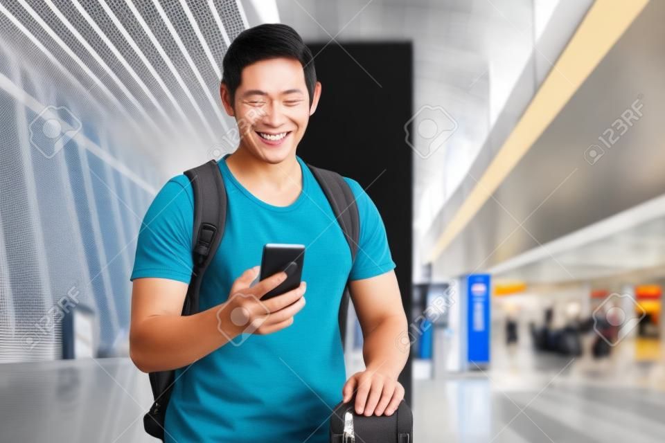 Gelukkige aziatisch toerist met telefoon en koffer op het vliegveld