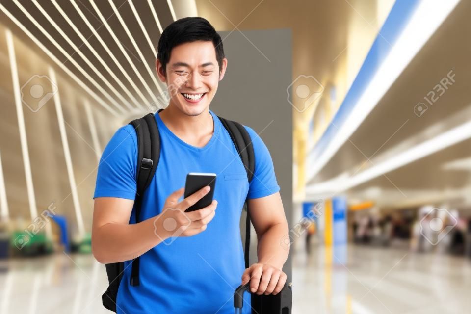 Heureux touriste asiatique tenant le téléphone et la valise à l'aéroport