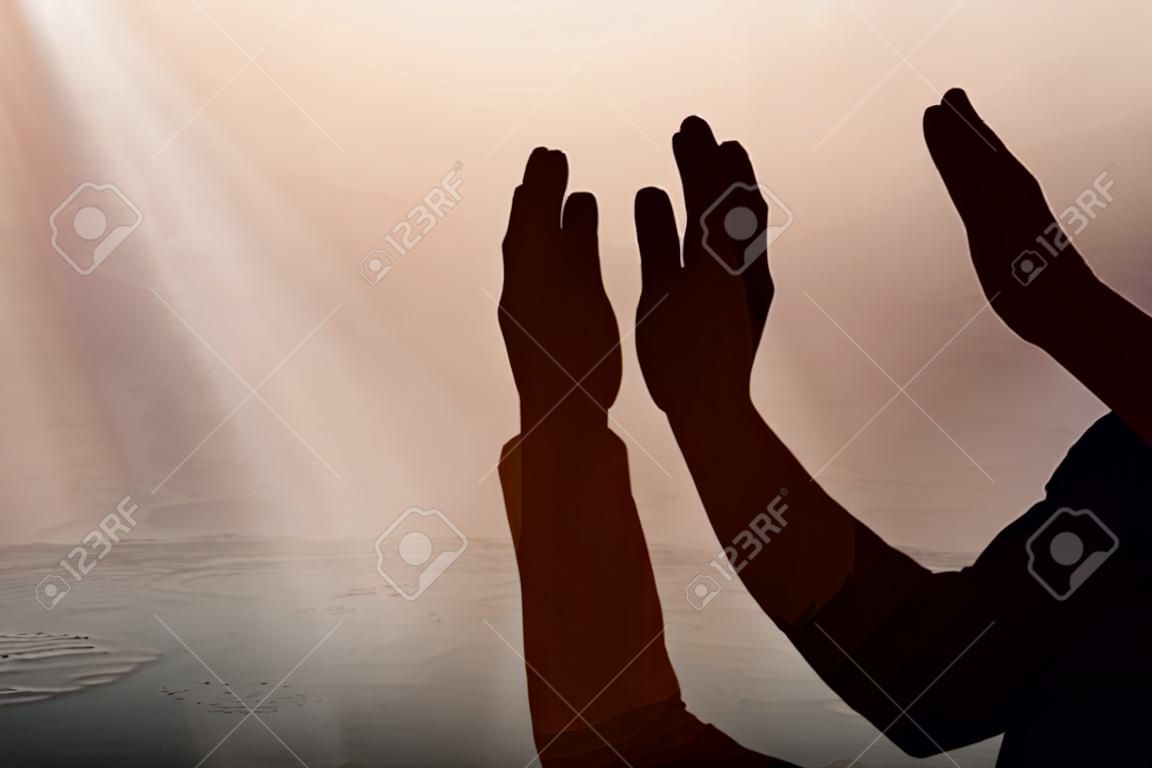 Silhouette di un uomo musulmano in piedi mentre alza le mani e prega con lo sfondo della scena notturna