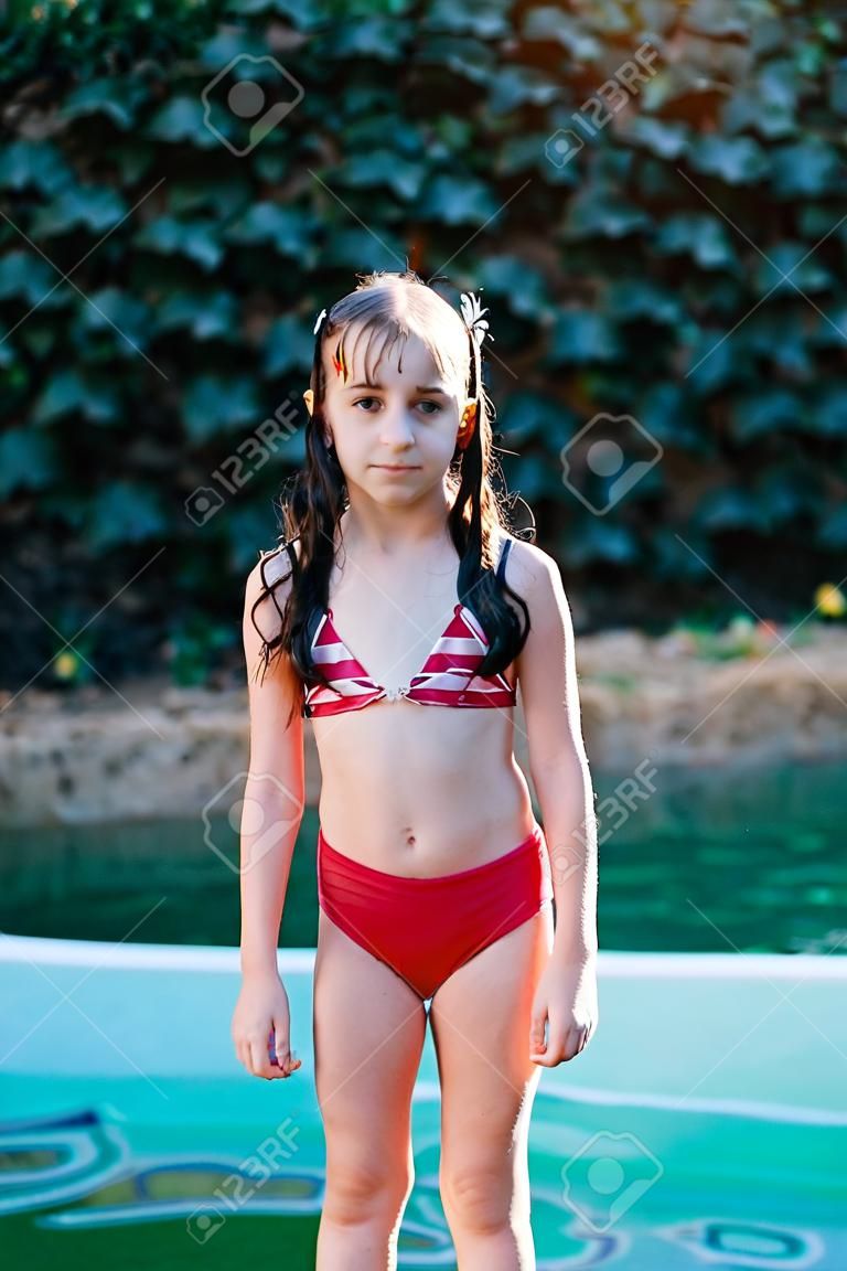夏の水着を着た女の子。日没。女の子 9 歳.ティーンエイジャー10歳。女子高生はプールで泳いでいた。森の中や新鮮な空気の中でプール。9歳の少女の肖像。夏はもうすぐ