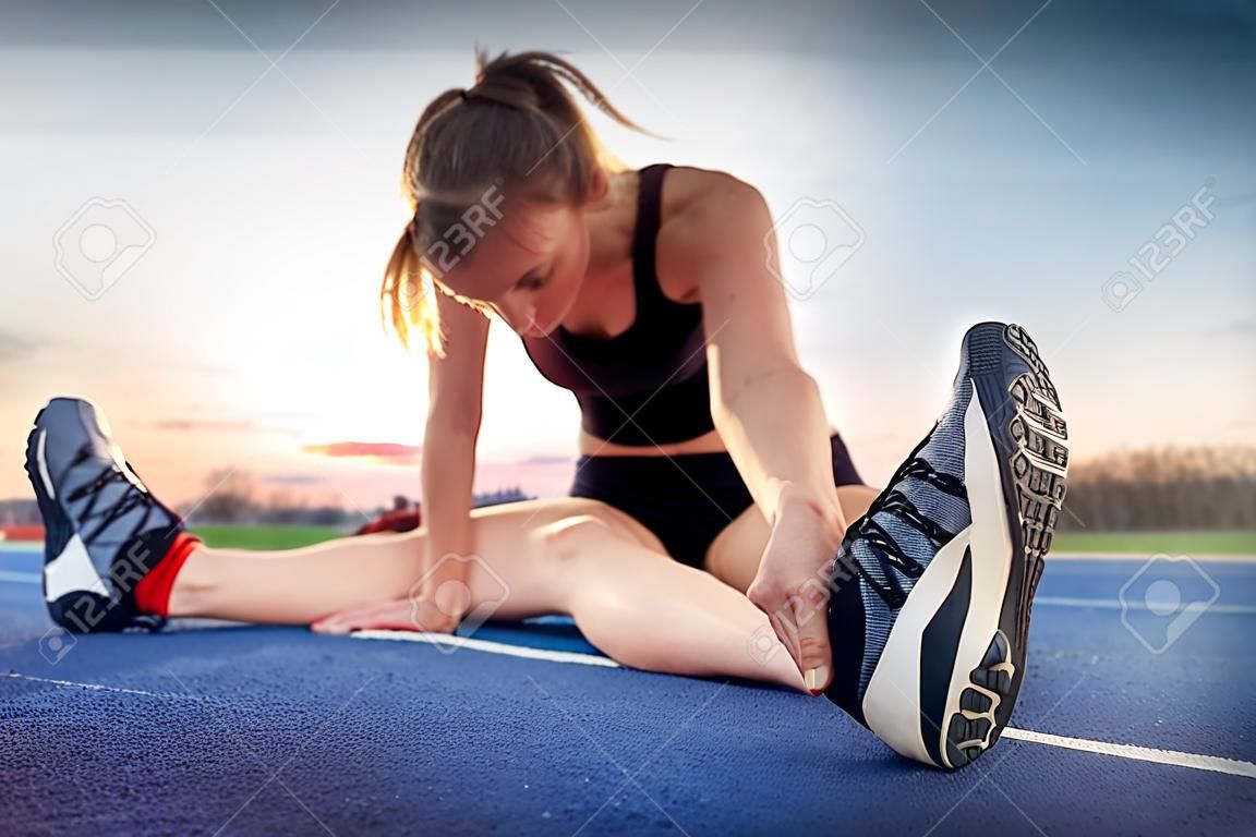 Athlete woman sitting on running track and stretching, feet close up