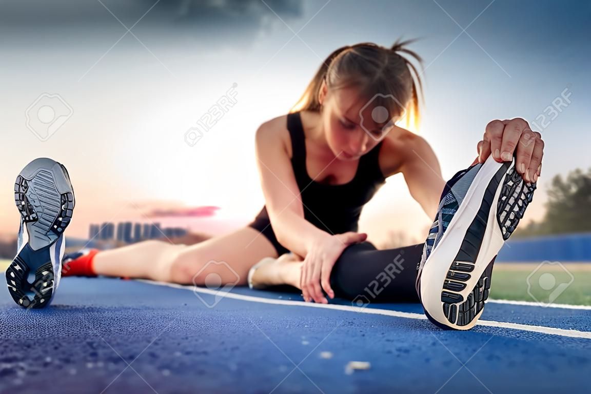 Athlete woman sitting on running track and stretching, feet close up
