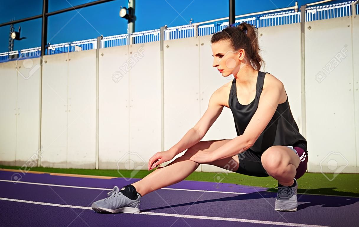 Athletic woman stretching on stadium running track