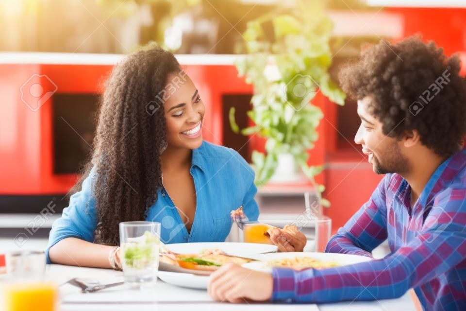 Glückliches junges Paar, das zusammen im Restaurant zu Mittag isst, afroamerikanische Leute, die Spaß haben?