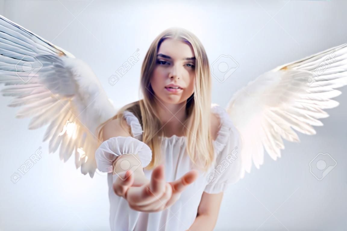 Een engel uit de hemel geeft je een hand. Jong, prachtig blond meisje in het beeld van een engel met witte vleugels.