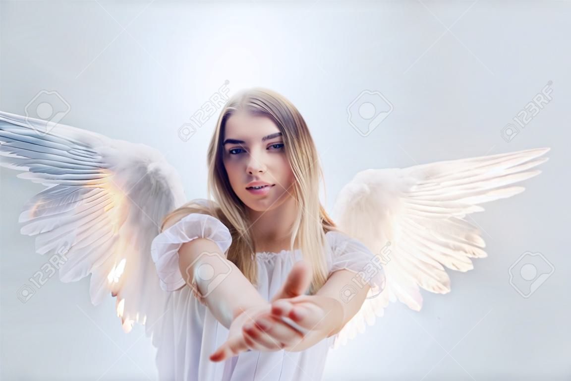 A mennyből származó angyal kezet nyújt neked. Fiatal, csodálatos szőke lány egy angyal képében, fehér szárnyakkal.