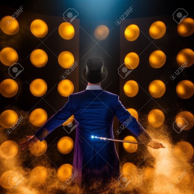 Showman. Young male entertainer, presenter or actor on stage. Back, arms to sides, smoke on background of spotlight