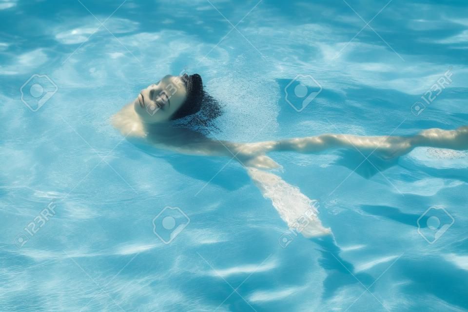 젊고 아름답고 날씬한 여성은 수영장에서 혼자 수영합니다. 스파 및 휴식, 고급 호텔. 물 위의 아름다운 갈색 머리 초상화, 클로즈업
