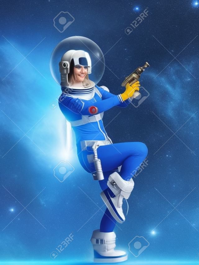 Fantástico disfraz de astronauta al estilo retrofuturista. una joven rubia hermosa con un traje azul con una esfera y un casco con un blaster en la mano. pionero de la exploración espacial, era atómica, estilo retro