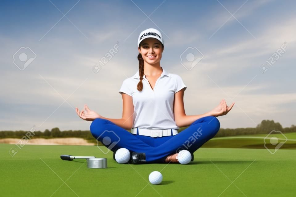 Mädchengolfer, der in Yogahaltung auf Golfplatz sitzt.