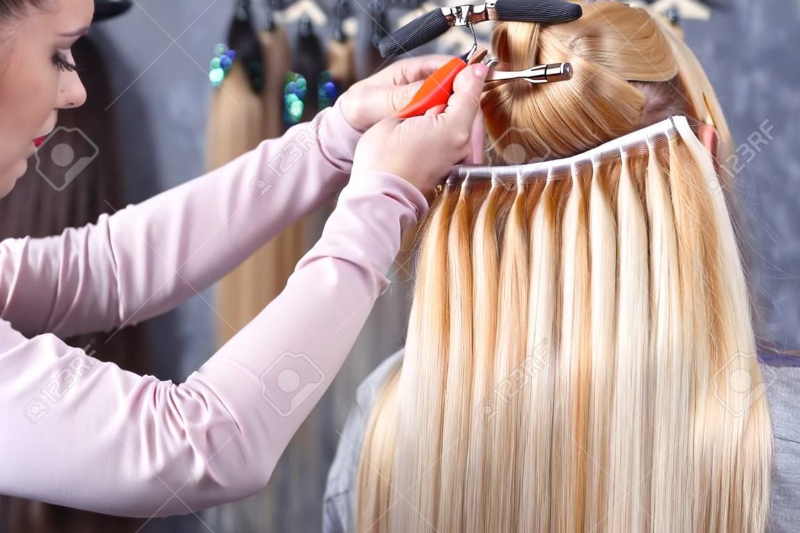 Procédure d'extension des cheveux. Le coiffeur fait des extensions de cheveux à une jeune fille, blonde dans un salon de beauté. Mise au point sélective.