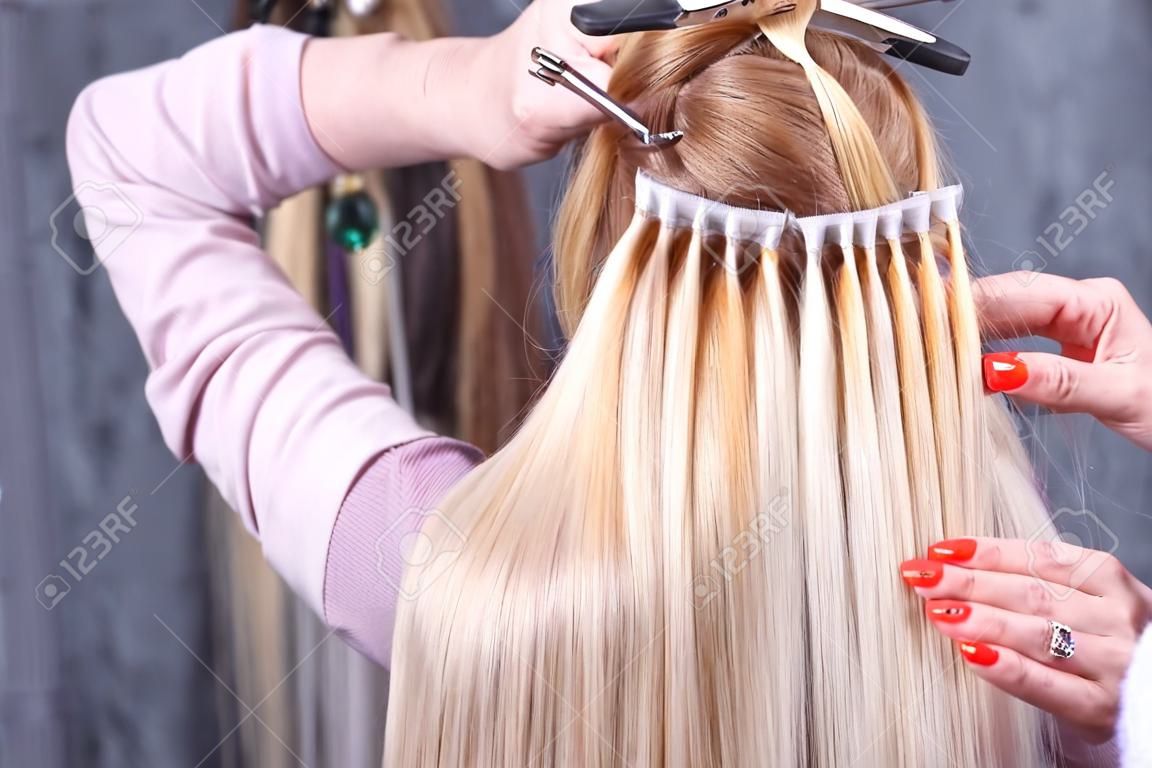 Haarverlängerungsverfahren. Friseur macht Haarverlängerungen zum jungen Mädchen, Blondine in einem Schönheitssalon. Selektiver Fokus
