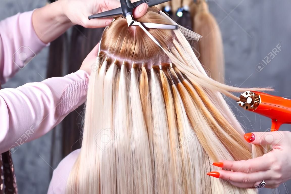 Haarverlängerungsverfahren. Friseur macht Haarverlängerungen zum jungen Mädchen, Blondine in einem Schönheitssalon. Selektiver Fokus