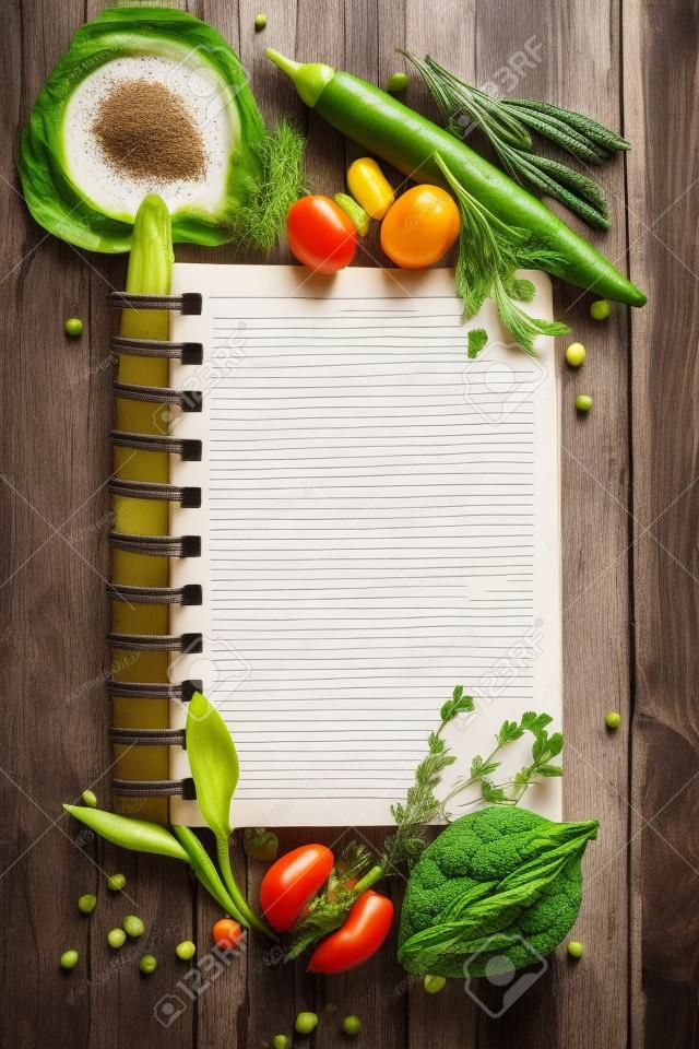 Open receptenboek met groenten en kruiden op een houten achtergrond.