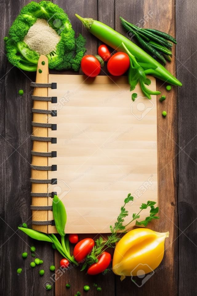 Open receptenboek met groenten en kruiden op een houten achtergrond.