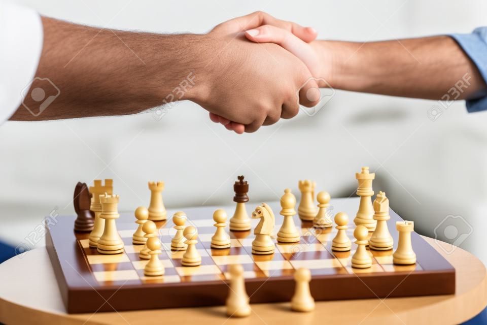 visão parcial de pai e filho apertando as mãos depois de jogar xadrez jogo de tabuleiro