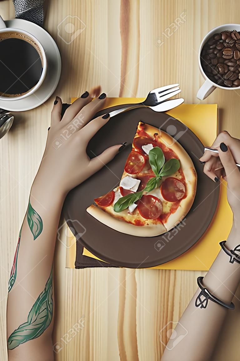 partial view of woman sitting at table with pizza piece on plate and cup of coffee