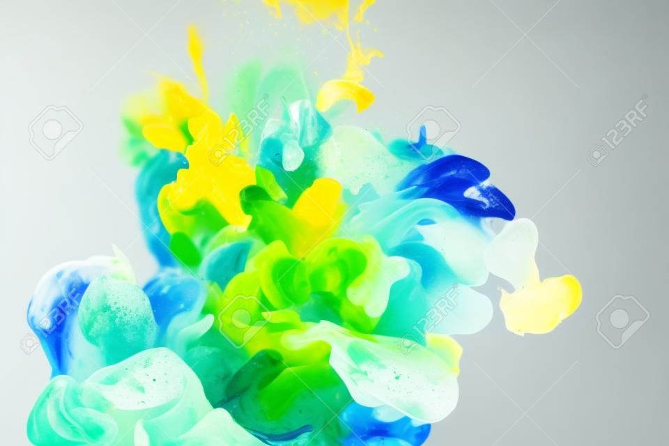 close up view of mixing of green, yellow and bright turquoise paints splashes in water isolated on gray
