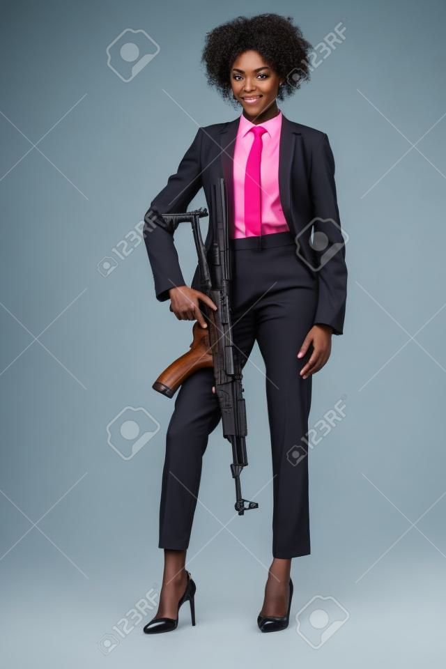 Femme afro-américaine espion en costume avec fusil, isolé sur blanc