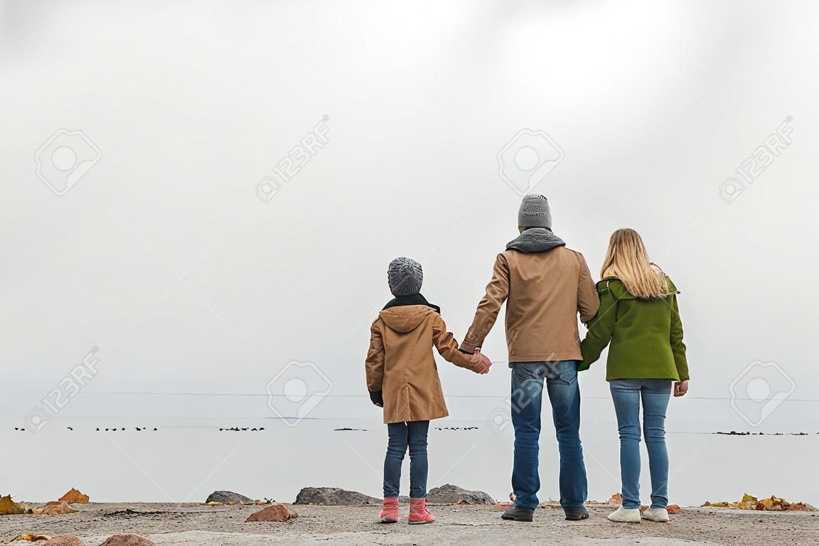 familie, die hände hält und an einem bewölkten herbsttag auf das meer blickt
