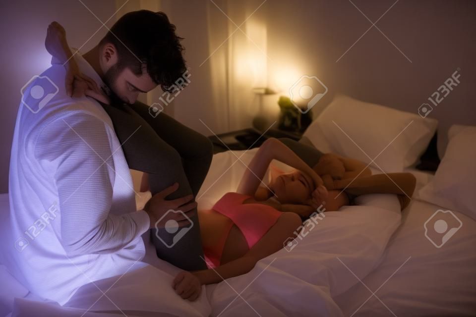 fiatal jóképű férfi megcsókolta barátnője lábát az ágyban a sötét szobában
