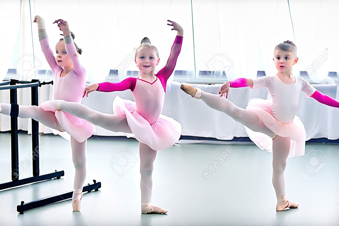 Hermosas pequeñas bailarinas de ballet haciendo ejercicio y mirando a la cámara en la escuela de ballet