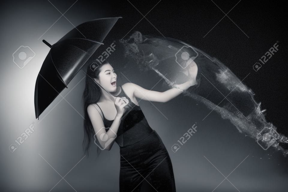 young emotional woman with umbrella swilled with water isolated on black