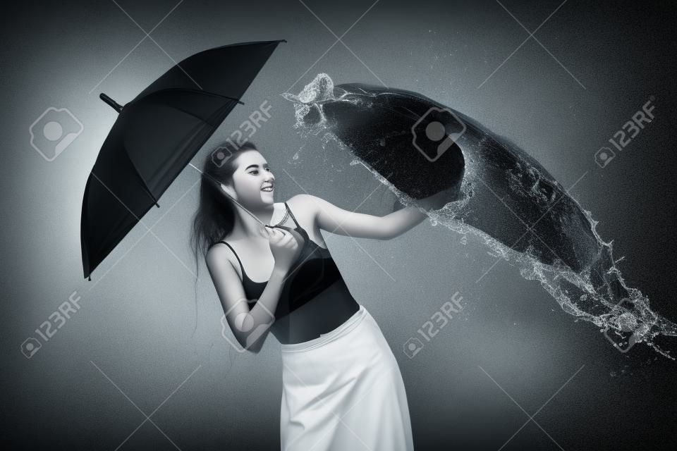молодая эмоциональная женщина с зонтиком, наполненная водой, изолированная на черном