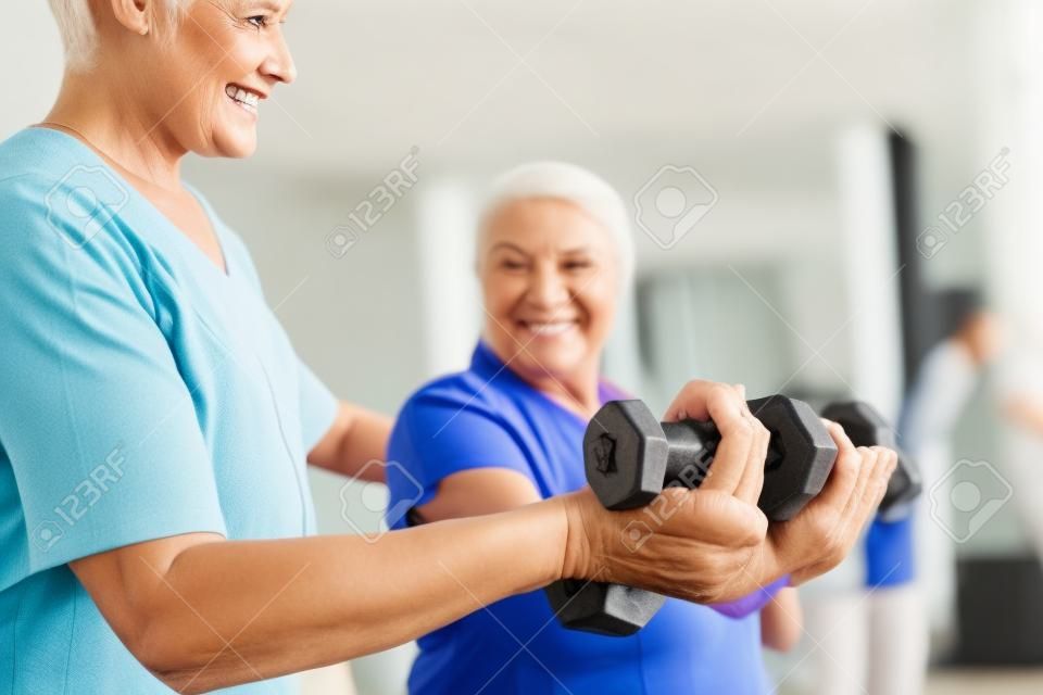 Zbliżenie pracownika socjalnego pomagającego uśmiechniętej starszej kobiecie ćwiczącej z hantlami