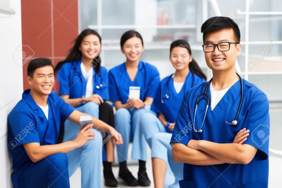 의과대학에서 백인 교사와 학생들 앞에 서 있는 아시아 남자