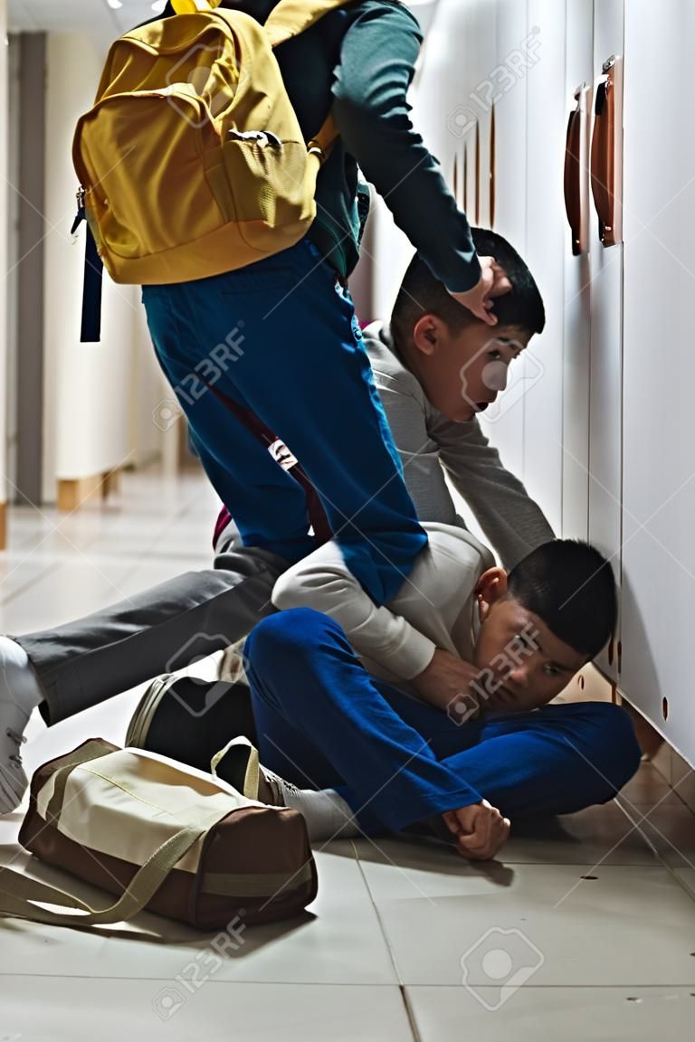 Frightened Asian schoolboy being bullied in school corridor