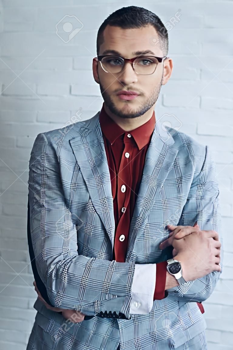 Attractive bearded man wearing suit and glasses in front of white wall