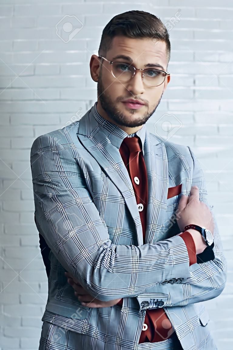 Attractive bearded man wearing suit and glasses in front of white wall
