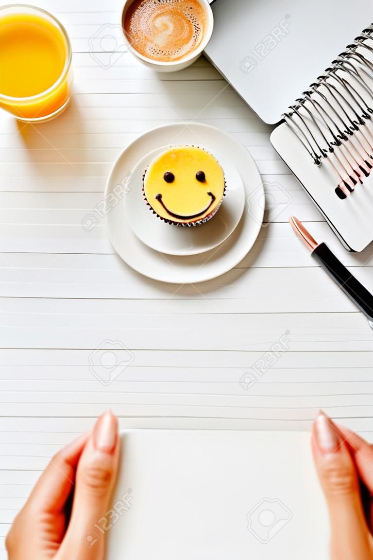 Cropped image of businesswoman holding empty visit card at table with orange juice, coffee cup and cake with symbol of smile in office